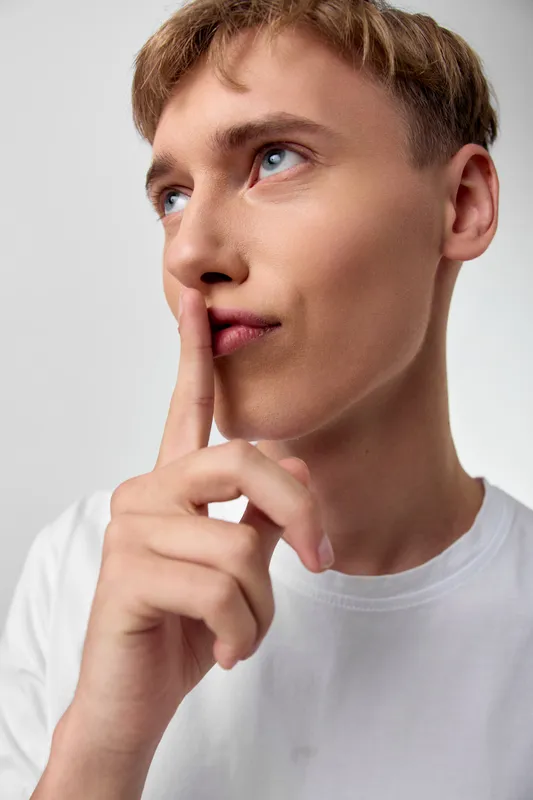 Thinking gesture with finger on lips signaling secrecy and quiet reflection in a simple white tee, studio lighting, calm mood and thoughtful focus