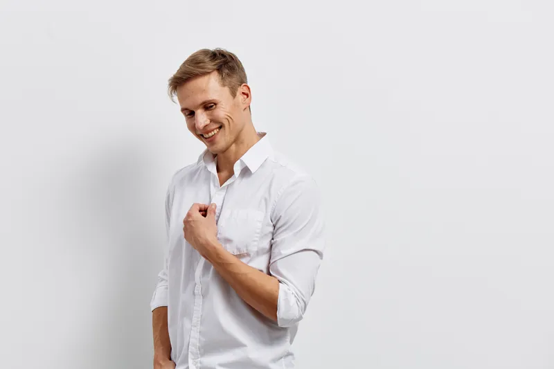 Friendly smiling young man in white shirt expressing happiness and confidence isolated on plain white background studio portrait. People lifestyle concept, positive attitude and success.