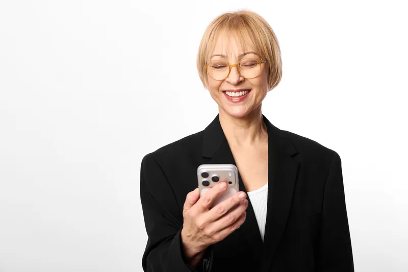 Woman smiling with eyes closed holding smartphone, business blazer portrait on clean white background, relaxed communication modern technology, copy space