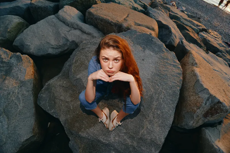 lifestyle woman in modern boho-western denim street style sitting on rocks outdoors with film color effect and relaxed confident expression