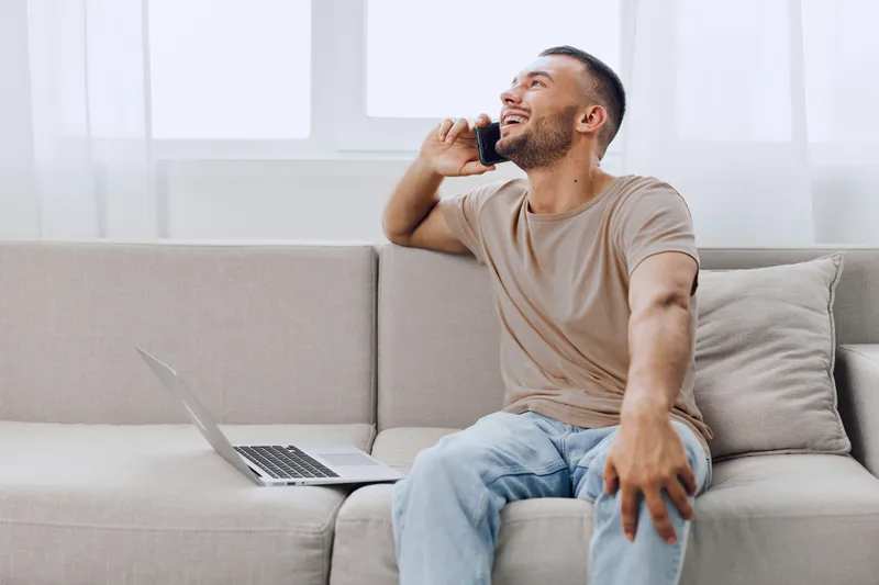Laughing man on a phone call, embracing soft masculinity and male vulnerability while enjoying a solo living moment in a cozy environment.