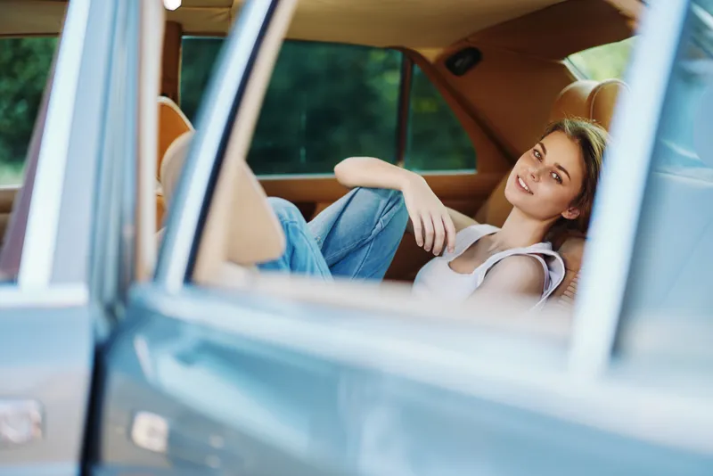 Beautiful young woman relaxing in a luxury car, wearing casual clothing and a bright smile, with a soft focus on the green background.