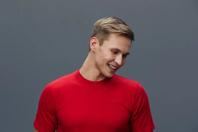 Smiling man with short gray hair wearing a vibrant red sweater poses happily against a plain gray background, showcasing a joyful expression, casual style, and relaxed mood. Studio portrait of a cheer