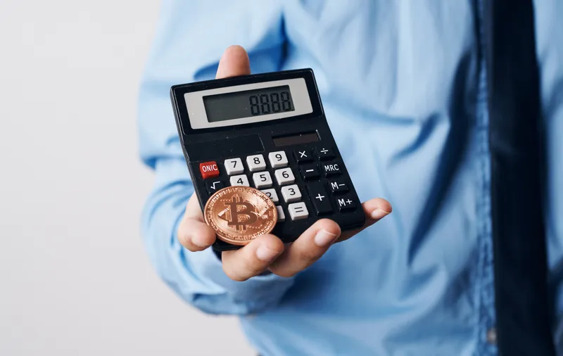 Мужчина держит в руках криптовалюту Bitcoin, калькулятор роста цены, финансовые технологии