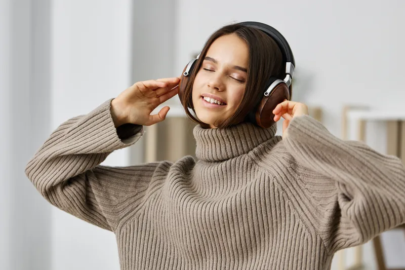 Улыбающаяся молодая женщина в наушниках слушает музыку на смартфоне, сидя дома