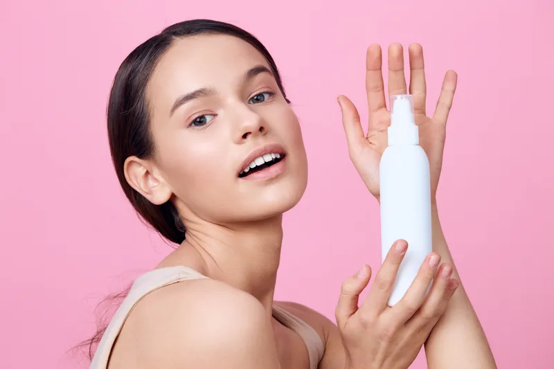 Young woman showcasing a skincare product against a pink background, highlighting beauty and self care with a joyful expression, perfect for health and beauty themes