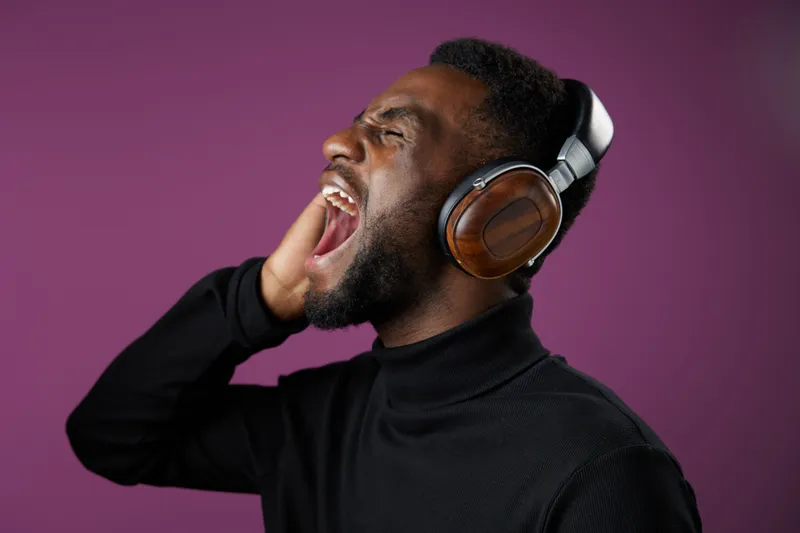 Black man in a stylish turtleneck passionately singing along with headphones, expressing joy and music enthusiasm against a vibrant purple background