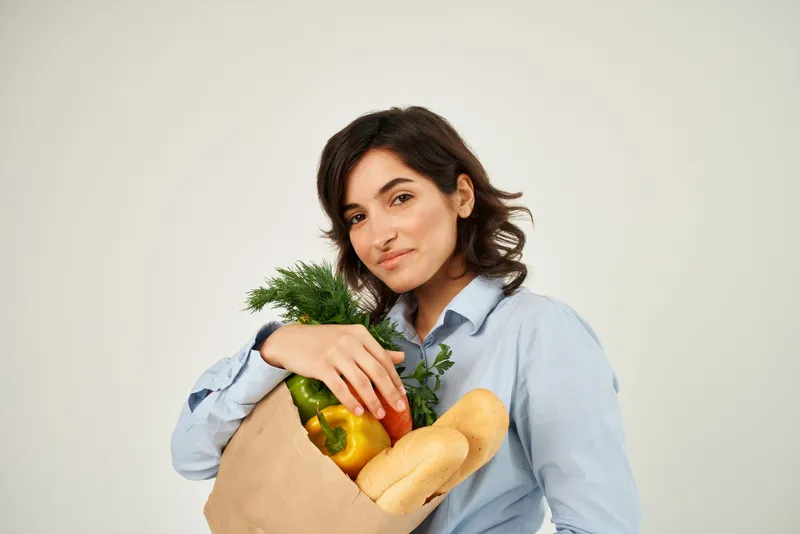 Брюнетка с пакетом продуктов, в котором находятся овощи, ассоциирующиеся со здоровым питанием, в супермаркете