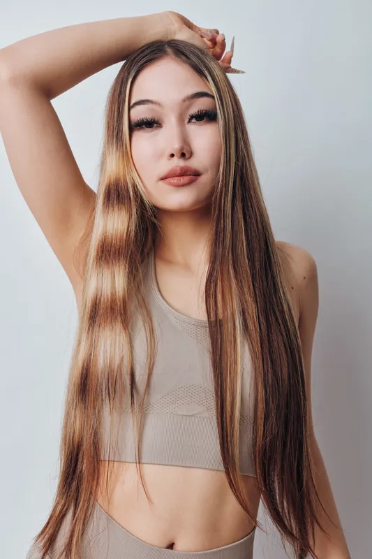 Portrait of young woman with long straight hair wearing beige crop top posing with hand on head isolated on white background. Beauty, fashion and hairstyle concept with confident model.