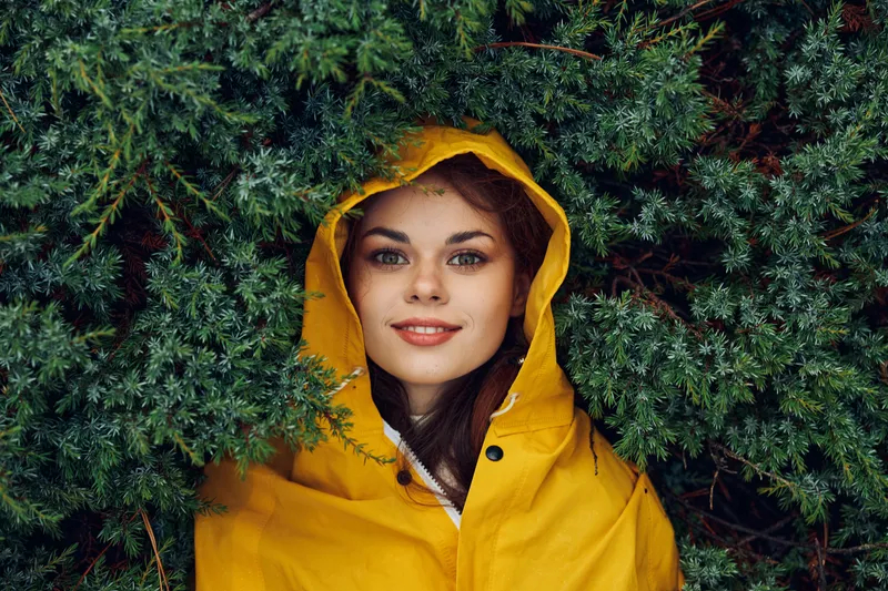 Женщина в жёлтом дождевике, окружённая пышной зеленью в мирной лесной обстановке во время спокойного побега на природу