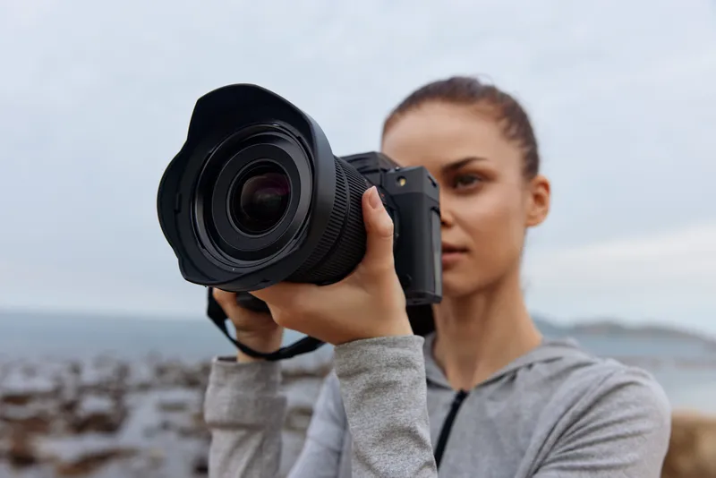 Young woman with a camera capturing coastal landscapes on a cloudy day, evoking creativity and adventure