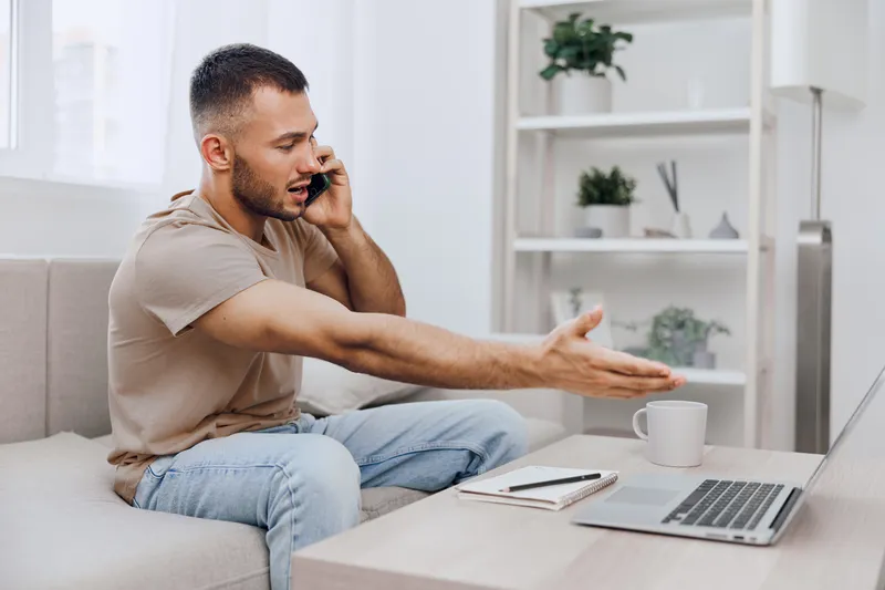 Engaged man on a phone call, expressing emotions with gestures, in a modern home office setting, showcasing productivity and communication.