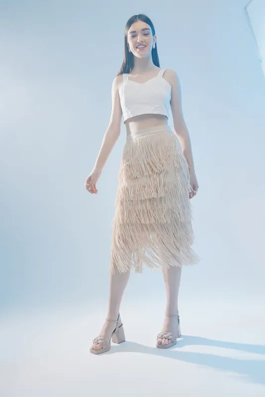 Young woman beauty fashion model posing in a white crop top and fringed skirt. Studio shot with soft lighting on a light background. Concept of style, elegance, and modern trends.