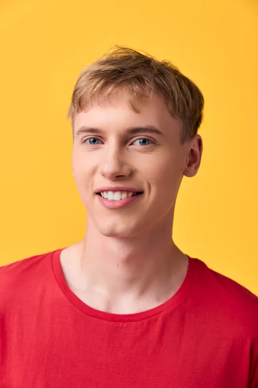 Smile, youth, man in a red shirt against a bright yellow background, conveying approachable casual style, warmth and friendly energy suitable for lifestyle, advertising or product presentation