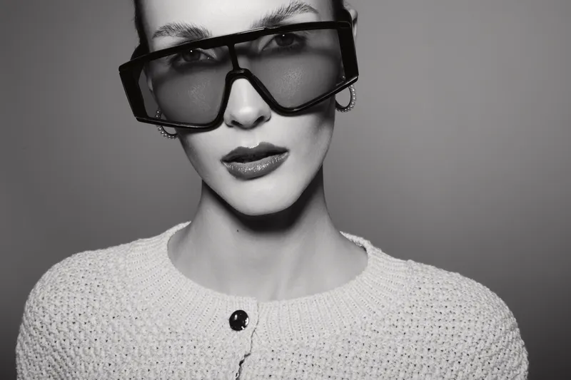 Close-up portrait of a fair skinned Caucasian woman wearing large sunglasses and a knitted sweater. Studio shot with soft lighting and neutral background for fashion concept.