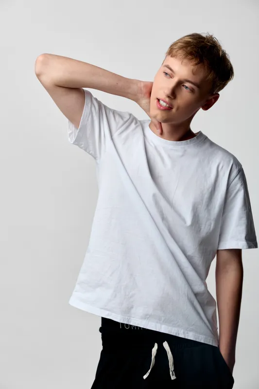Stretching neck and shoulder in a casual indoor pose, man wearing a white tshirt, relaxed stance, simple studio setting, soft lighting, everyday lifestyle moment that conveys comfort, flexibility,