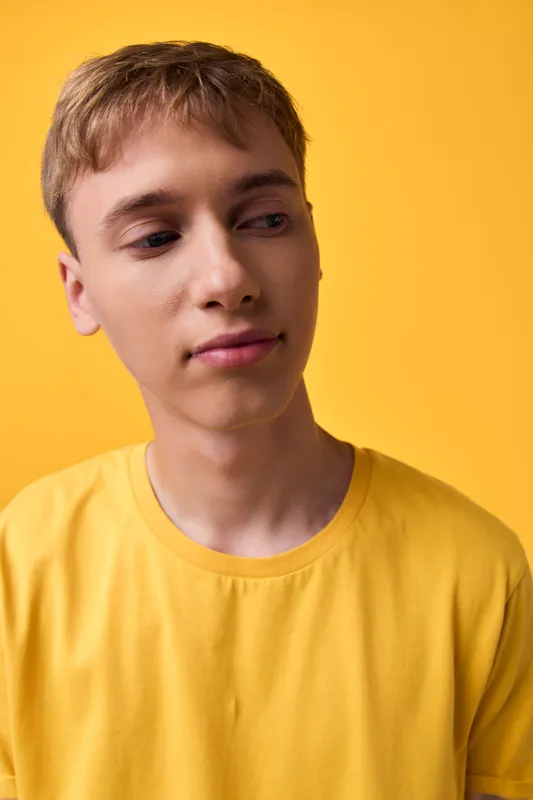 Young man wearing a yellow shirt stands against a yellow backdrop in a studio shot, capturing a casual mood, calm expression, and contemporary lifestyle style for branding or editorial use.