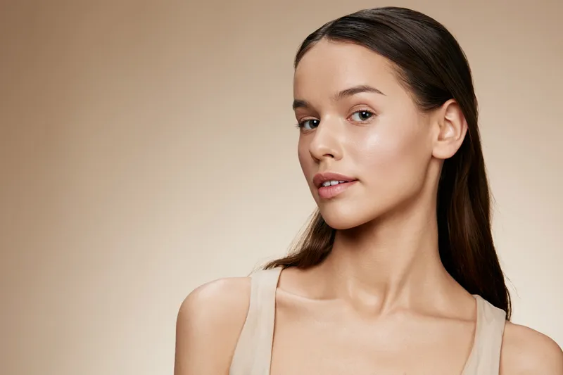Beautiful young woman with natural makeup and glowing skin against a soft beige background, exuding confidence and serenity Perfect for wellness and beauty themes