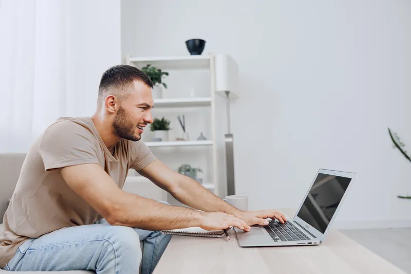Smiling man focusing on laptop, creating a productive workspace with modern decor and natural light enhancing his concentration and positivity.