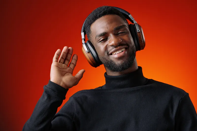 Smiling young man with headphones against an orange background, expressing joy and excitement in a modern and vibrant setting