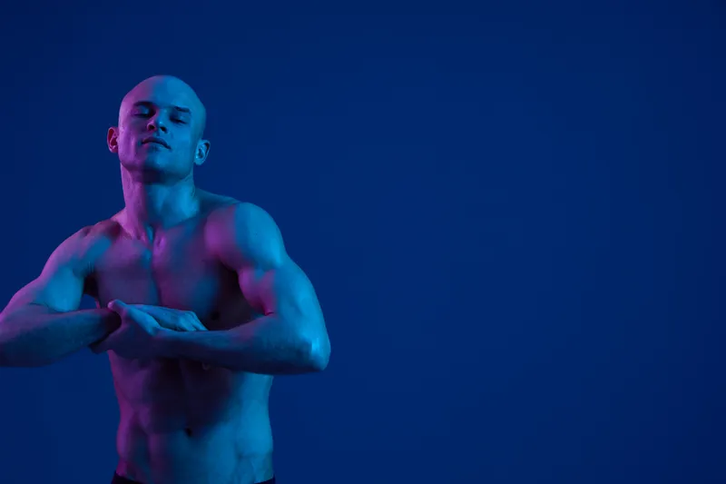 Confident man posing in a striking blue light, showcasing a powerful physique. This image emphasizes strength and intensity, ideal for fitness and sports themes.