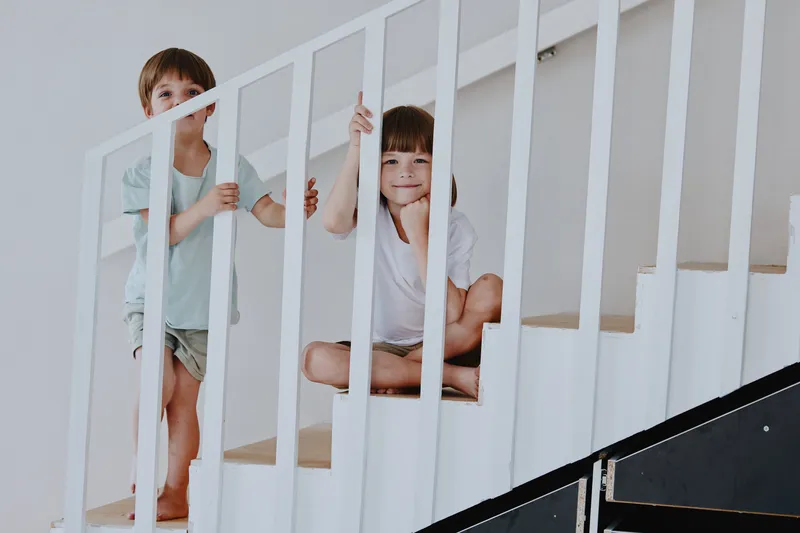 Two cheerful children exploring a bright, modern staircase, showcasing their playful spirit and natural curiosity in a cozy environment.