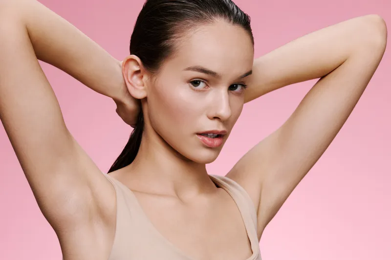 Confident young woman with sleek hair on a pink background showcasing beauty and self care, emphasizing skincare, femininity, and modern trends