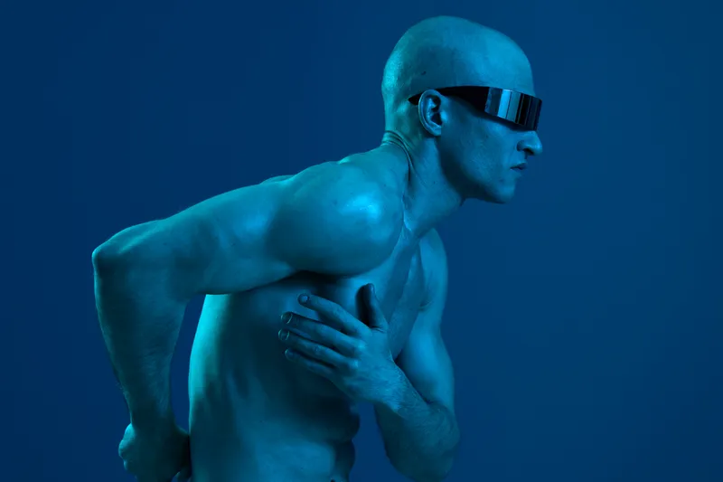 Man in futuristic sunglasses with blue lighting, expressing tension, showcasing a dynamic pose. This striking image emphasizes emotion and style in a captivating way.