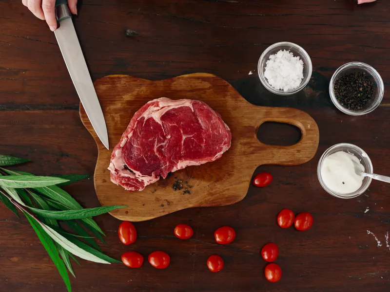 Женщина с ножом в руке нарезает свежее мясо стейка для жарки на кухне