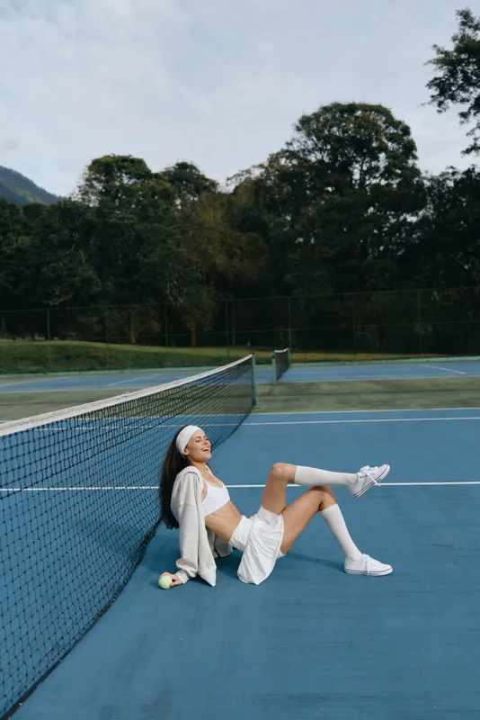 Young female tennis player enjoying her break on a blue court, wearing a sporty outfit and white sneakers, radiating joy and relaxation during sunny weather