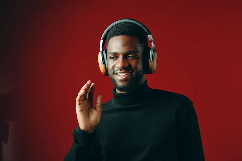Young Black man wearing headphones smiling against a red background, showcasing a joyful expression and modern fashion style