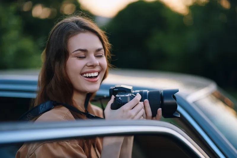 Cheerful young woman taking photos with a camera, enjoying nature, embracing creativity and outdoor exploration in a vibrant setting.