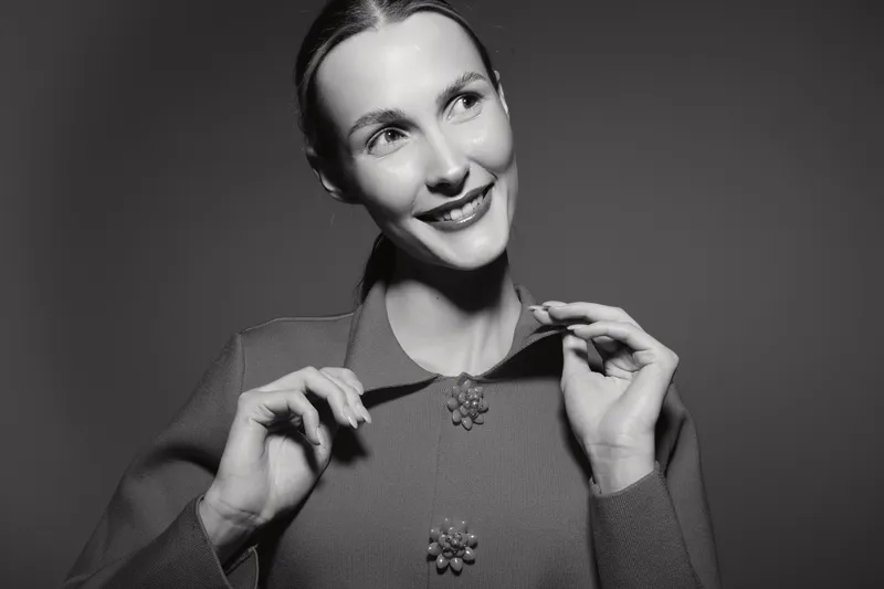Smiling caucasian woman with light skin wearing vintage clothing looks away in black and white studio portrait.