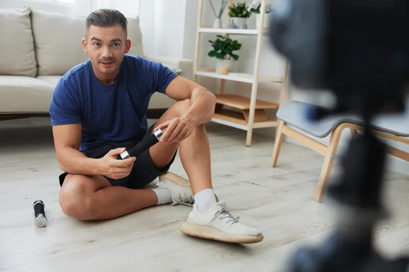 Мужчина-спортсмен, ведущий блог, записывает на камеру свои тренировки с гантелями для тела в домашних условиях