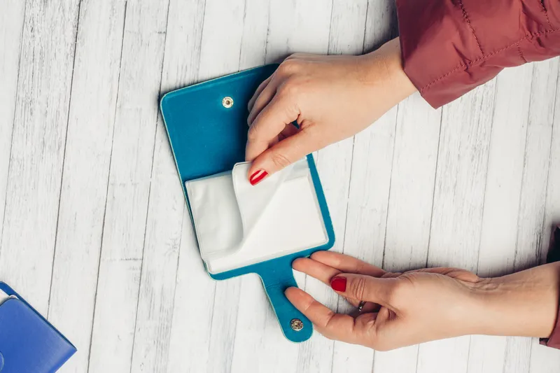 Синяя визитница в женских руках на деревянном столе, вид сверху