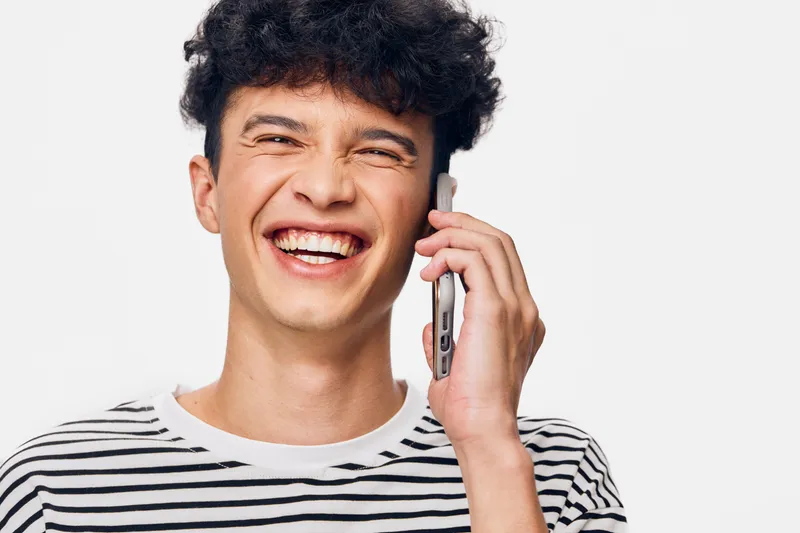 smiling man talking on smartphone in striped shirt with curly hair, joyful facial expression, isolated white background, casual communication concept