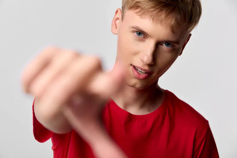 Close up of a confident young man in a red shirt reaching toward the camera, creating a dynamic sense of action, engagement and intensity, with strong stance and direct gaze.