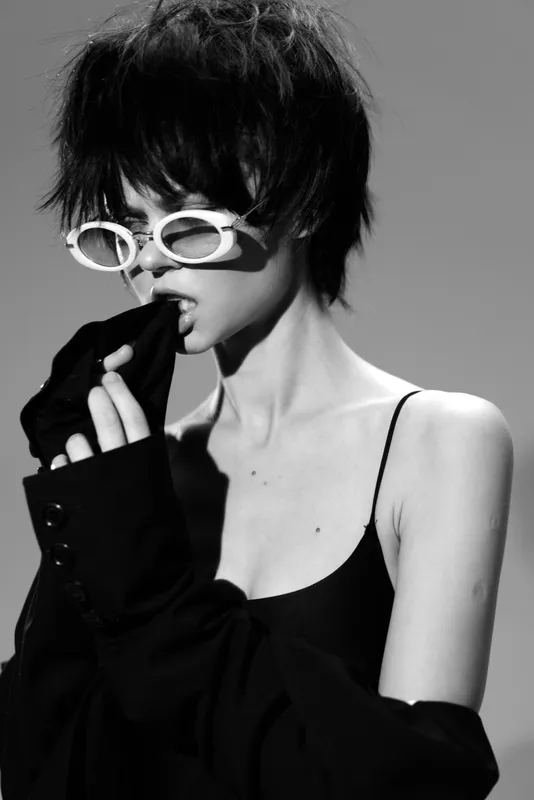 Black and white portrait of a stylish woman wearing sunglasses and a dark outfit with edgy vibe and confident attitude