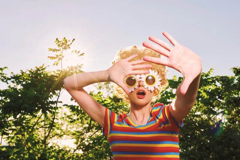 Playful child outdoors, wearing striped shirt and oversized sunglasses, sunlit moment with carefree laughter, colorful scene enhanced by retro film color vibe and soft breeze