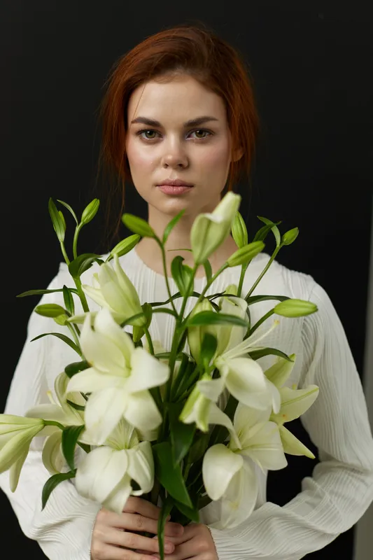 Young woman holding white lilies against a dark background, displaying a serene expression and highlighting the beauty of nature and peace