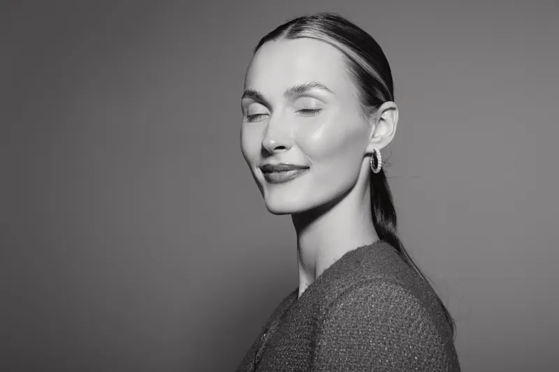 Portrait of a smiling Caucasian woman with light skin and closed eyes wearing earrings and a textured sweater. Concept of happiness, calmness, and natural beauty in studio lighting.
