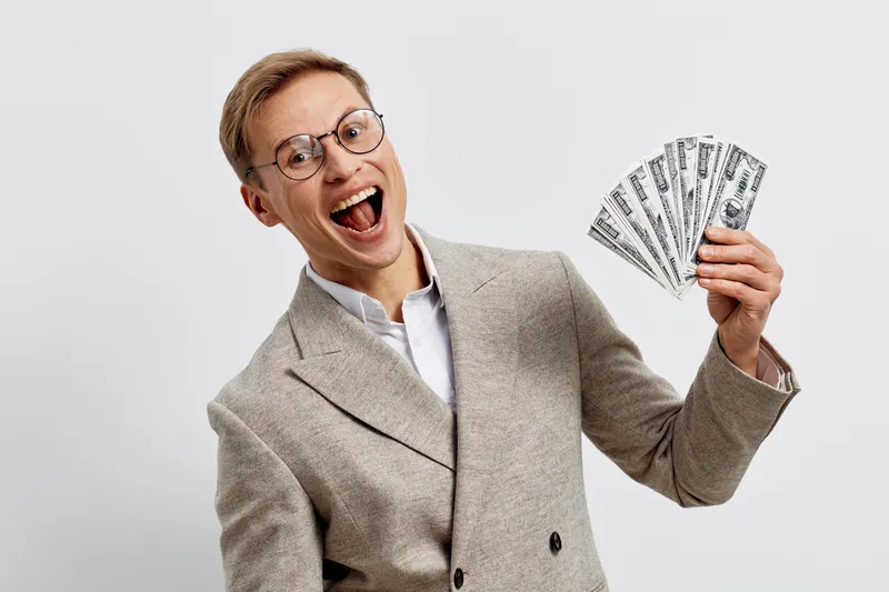 excited young caucasian man wear beige plaid jacket hold us dollar bills celebrate success internet freelancing work digital nomad concept