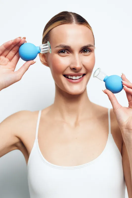 Woman face massage skincare beauty spa relaxation self care wellness portrait, smiling young woman uses blue massage balls on cheeks for a gentle skincare routine daily
