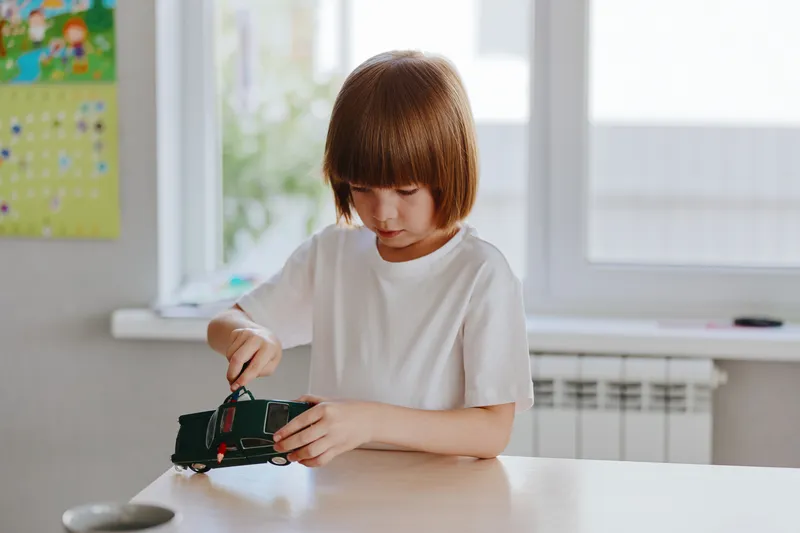 Young boy playing with a toy car, focused on his activity. Bright indoor setting enhances creativity and playfulness, showcasing childhood joy and imagination.