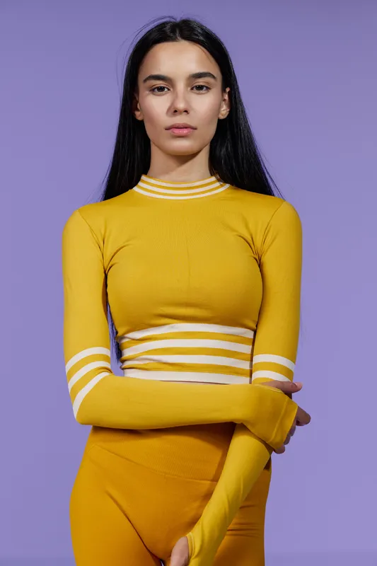 Young woman sport fitness dressed in yellow activewear stands confidently against purple background, showing strength, determination, and focus in modern athletic style.