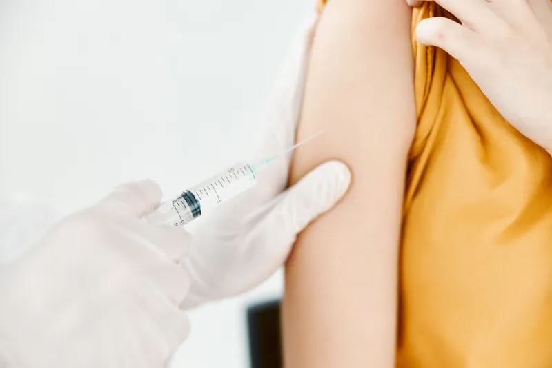 Врач делает женщине укол в плечо вакциной от COVID-19