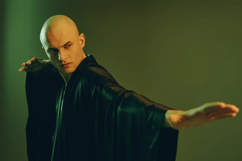 Energetic man in black robe striking a powerful pose, showcasing strength and focus in a creative setting. Unique lighting enhances the dramatic effect.