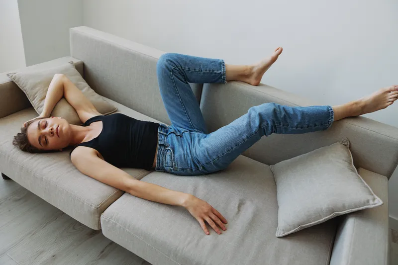 Молодая женщина с короткой стрижкой веселится дома на диване, улыбается и излучает счастье