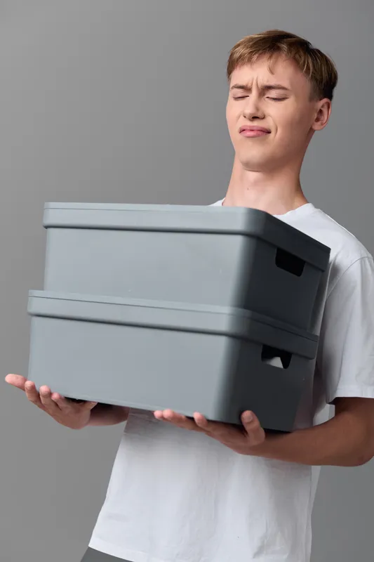 Man holding two gray storage boxes for moving and organization, simple home cleanup and tidy shelves, practical packing solution for home and workspace