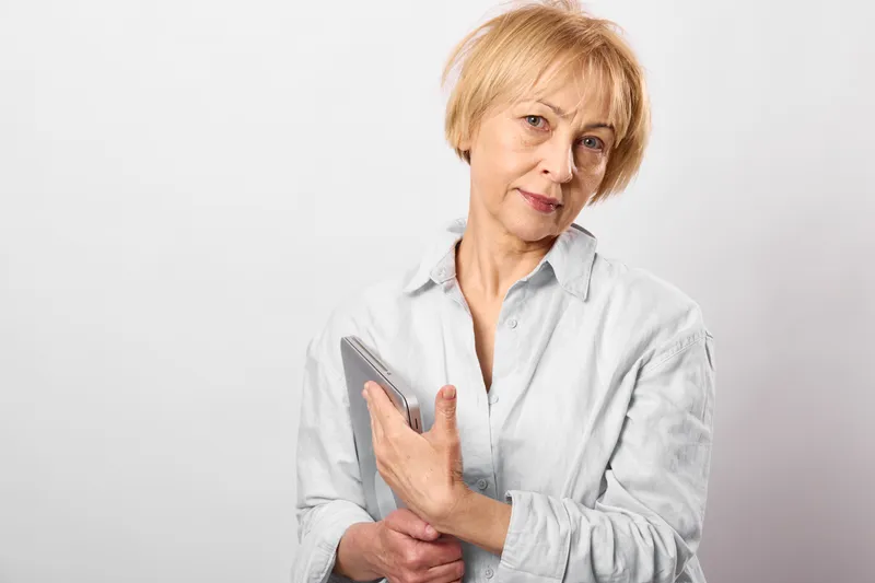 Elderly woman shows arthritis pain in her forearm while holding a smartphone, suggesting telehealth healthcare needs for medical diagnosis at home and selfcare support
